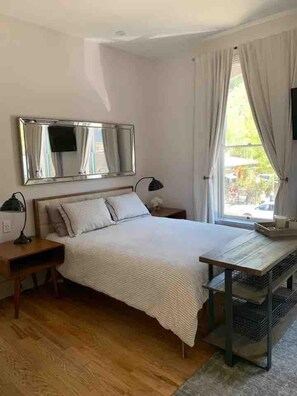 A bedroom with a bed, bedside tables, a mirror, a window with curtains, and a view of the outside. - Main Street Luxury in Heart of Telluride | Walk to Gondola and Explore Town (Telluride)