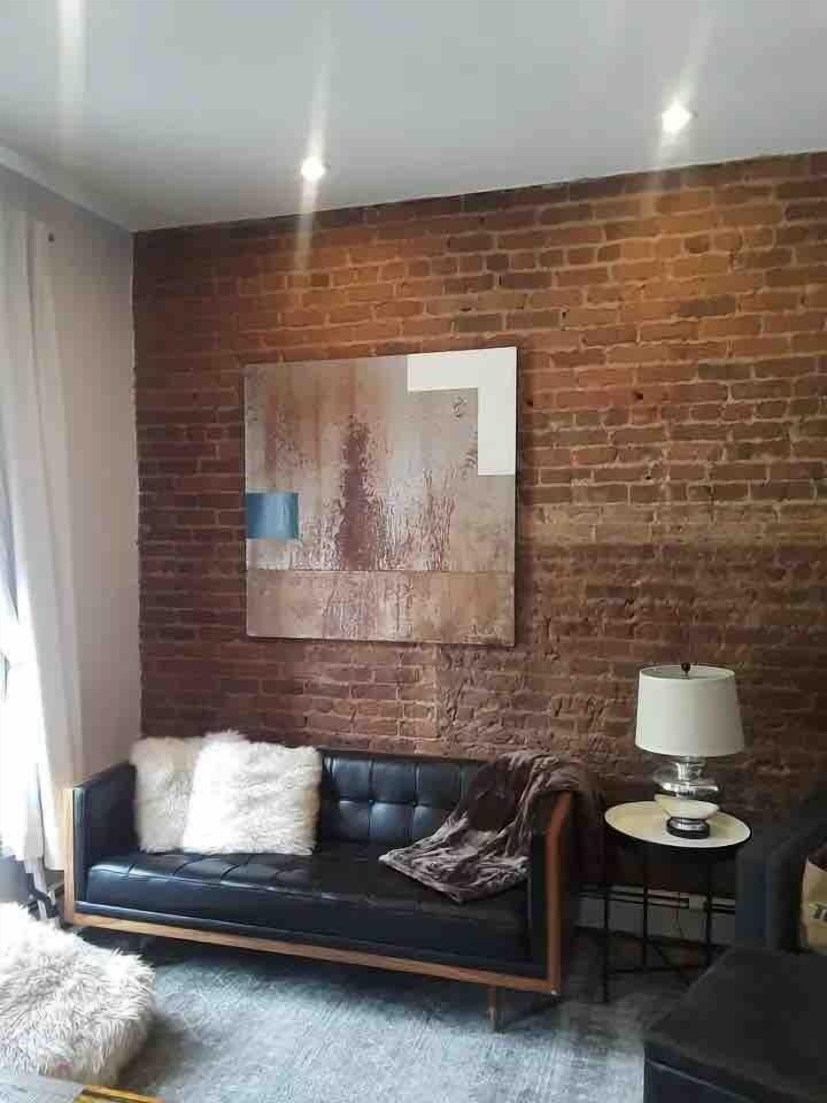 A living room with a brick wall, a sofa, a lamp, and a framed artwork.