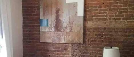 A living room with a brick wall, a sofa, a lamp, and a framed artwork.