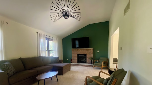Una sala de estar con un sofá modular, una mesa de centro redonda, una chimenea y un televisor montado en la pared.