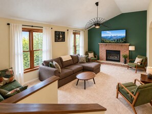 A living room with a sectional sofa, a fireplace, and a large window with curtains. - TNT Pocono Haven - 5BR - Sleeps 14 - Minutes from Kalahari (Pocono Summit)