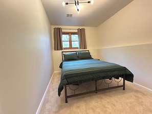 Ein Schlafzimmer mit einem Einzelbett, einem Fenster mit Vorhängen, einer Deckenleuchte und einem Teppichboden.