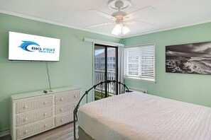A bedroom with a bed, a radiator, a window with blinds, a ceiling fan, and a wall-mounted TV displaying a logo. - Amazing 2BR Unit at A Place at the Beach with Pool (Myrtle Beach)