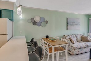 A dining area with a wooden table and chairs, a wall with decorative plates, and a sofa with a floral pattern. - Amazing 2BR Unit at A Place at the Beach with Pool (Myrtle Beach)