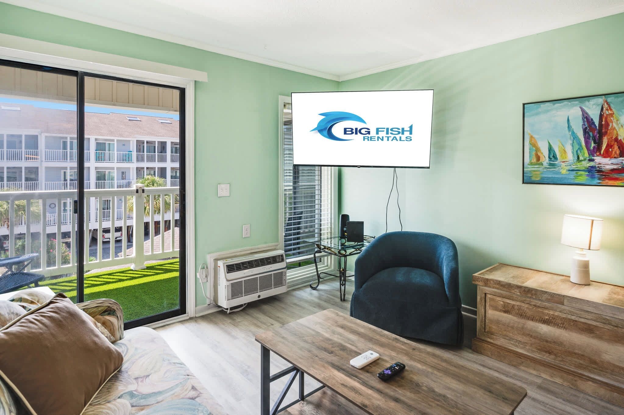 Een moderne woonkamer met een groot televisiescherm, een comfortabele bank, een houten salontafel en uitzicht op een groen gazon en gebouwen.