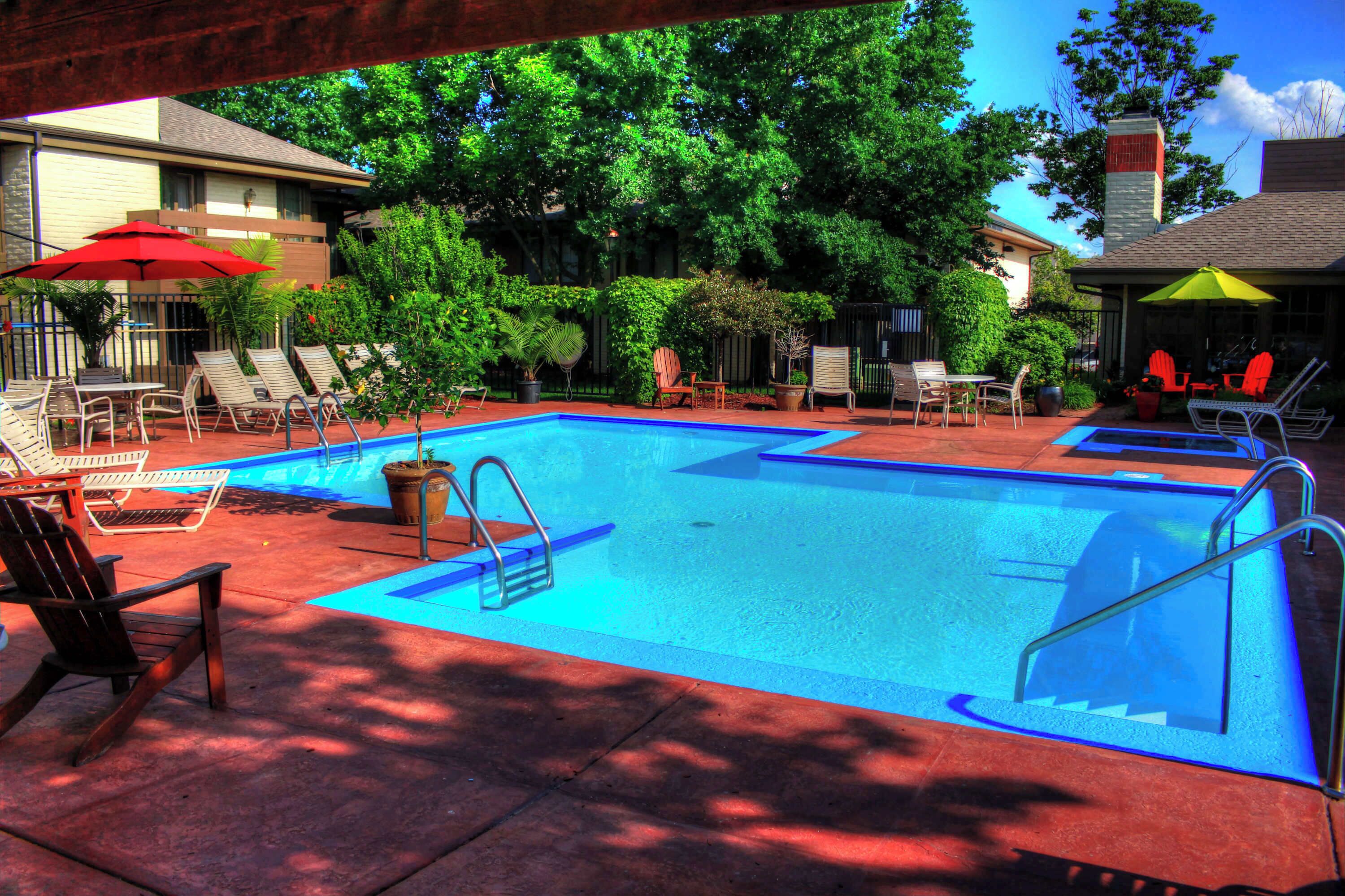 A swimming pool with lounge chairs and umbrellas, surrounded by trees and a building.