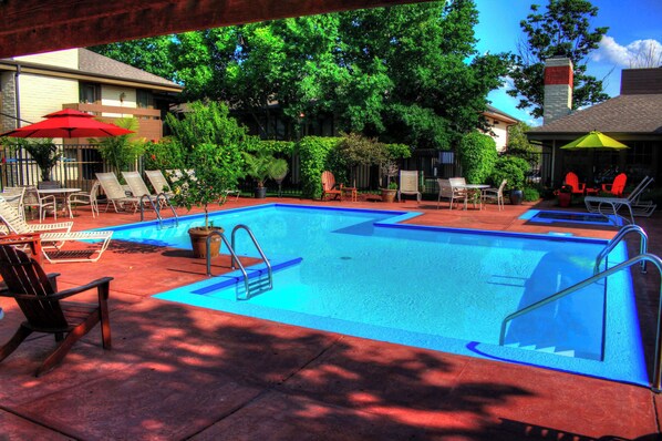 A swimming pool with lounge chairs and umbrellas, surrounded by trees and a building.