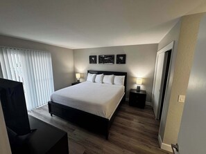 A bedroom with a bed, two bedside tables with lamps, a TV, and a door.