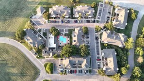 An aerial view of a residential complex with multiple buildings, a central swimming pool, and parking areas.
