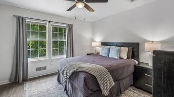 A bedroom with a bed, a nightstand, a dresser, a ceiling fan, and a window with curtains.