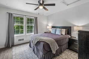 A bedroom with a bed, a nightstand, a dresser, a ceiling fan, and a window with curtains.