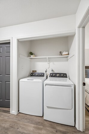 A laundry room with two front-loading washing machines and a shelf above them.