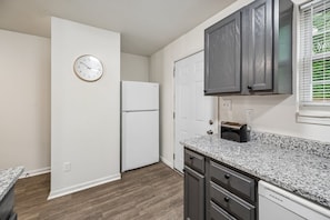A kitchen with a white refrigerator, a clock on the wall, and a window with blinds.