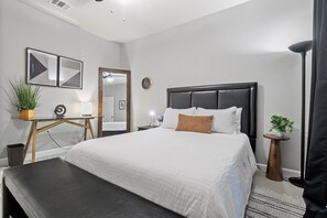 Ein modernes Schlafzimmer mit einem großen Bett, einem Schreibtisch, einem Spiegel und einer Topfpflanze.