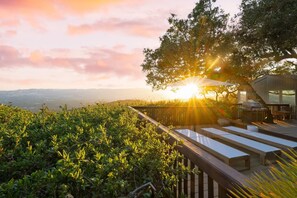 Una terraza con mobiliario exterior y zona de barbacoa, con vistas a un viñedo y un paisaje distante.