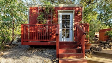 Una pequeña estructura de madera roja con una puerta blanca y una escalera de madera que lleva hacia ella.