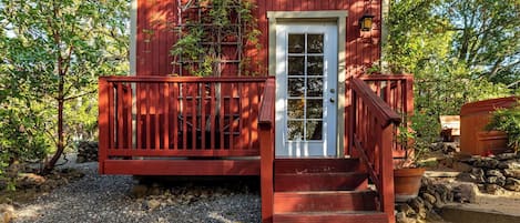 Una pequeña estructura de madera roja con una puerta blanca y una escalera de madera que lleva hacia ella.