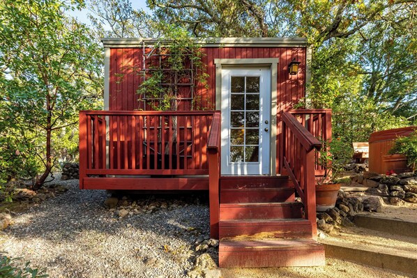 A small red wooden structure with a white door and a wooden staircase leading up to it.