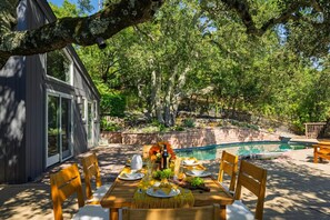 A dining area with a table set for four, surrounded by wooden chairs, with a pool and a stone wall in the background. - Sonoma Skyhouse l Pool Hot Tub Sauna Views (Sonoma)