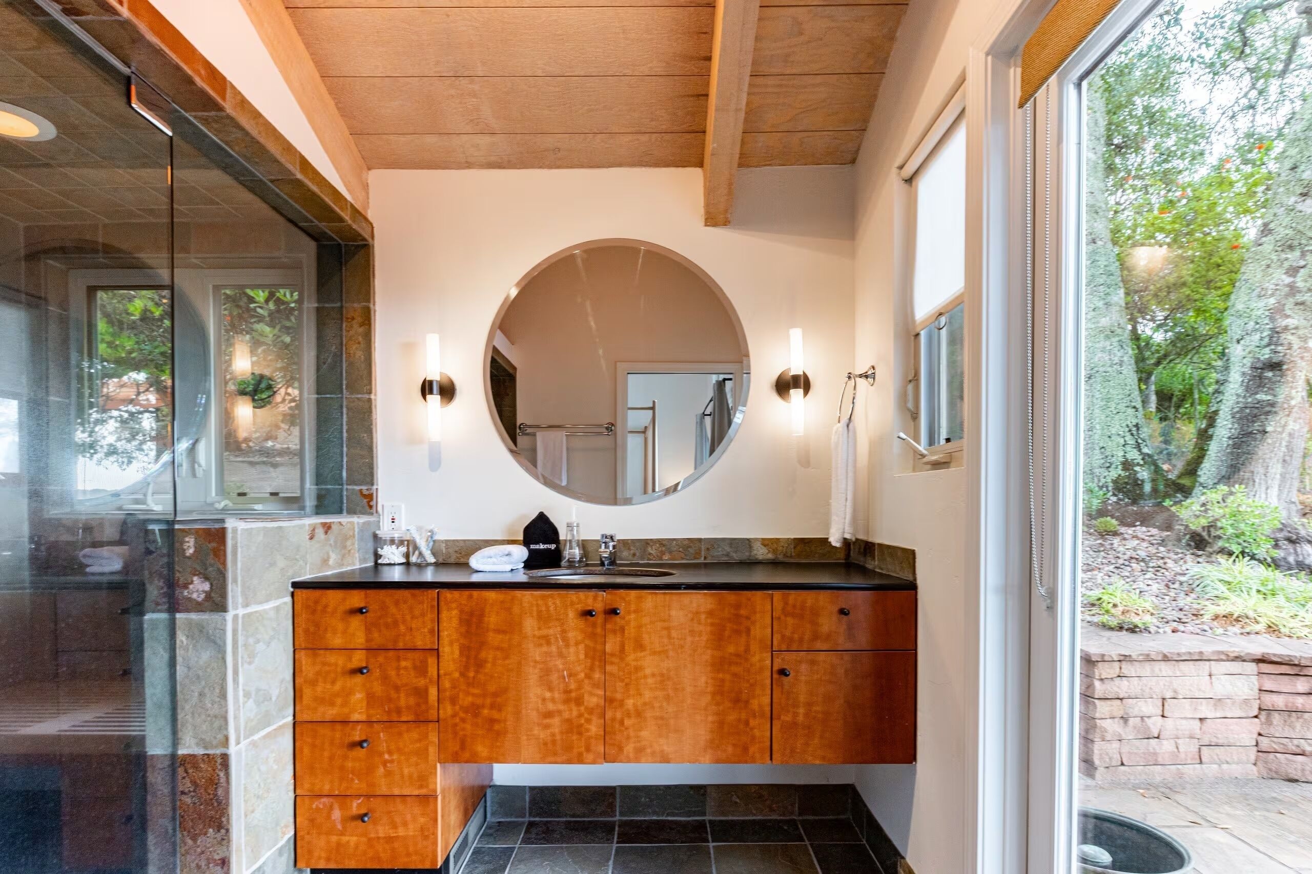 A bathroom with a wooden vanity, a round mirror, and a sink.