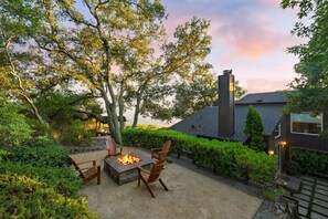 Une terrasse avec un foyer, des sièges et une vue sur une maison dotée d’une cheminée.