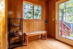 Un intérieur en bois avec un banc, une étagère où sont posés des sacs et une fenêtre donnant sur des arbres.