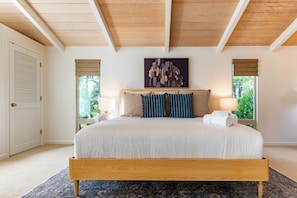 Une chambre à coucher avec un lit en bois, une grande fenêtre donnant sur un paysage verdoyant et un tableau accroché au-dessus du lit.