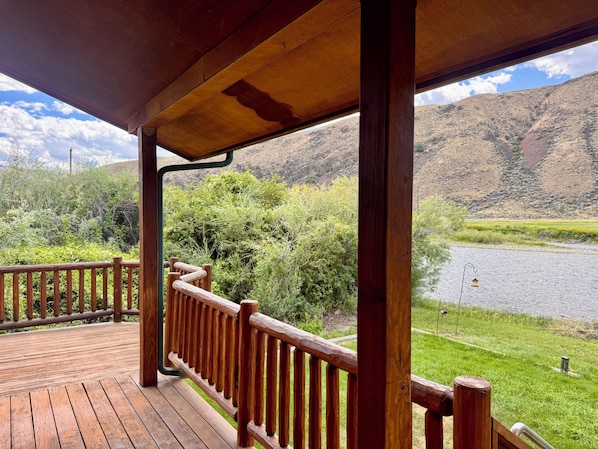 A wooden deck with a railing overlooking a river and hills.