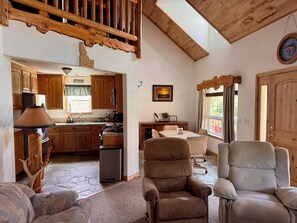A cozy living area with a fireplace, comfortable seating, and a view of the kitchen.