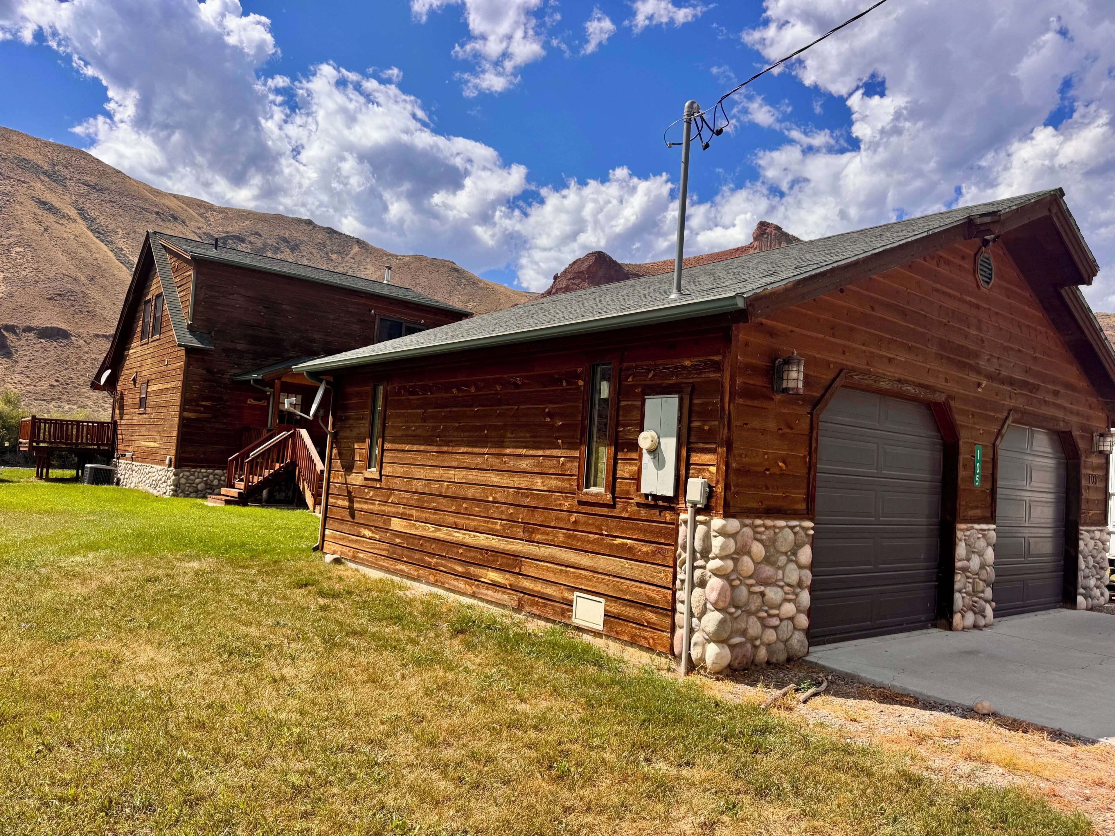 A wooden cabin with a stone foundation, a front porch, and a garage.