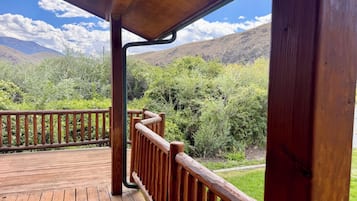 Varanda de madeira com guarda-corpo, com vista para uma paisagem montanhosa.