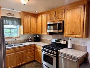 A kitchen with wooden cabinets, a stainless steel refrigerator, a microwave, a stove, and a coffee maker.