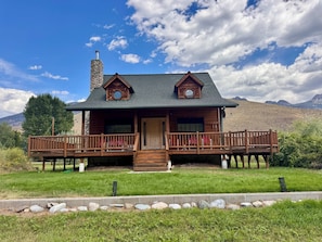 A wooden cabin with a porch, a chimney, and a view of mountains.