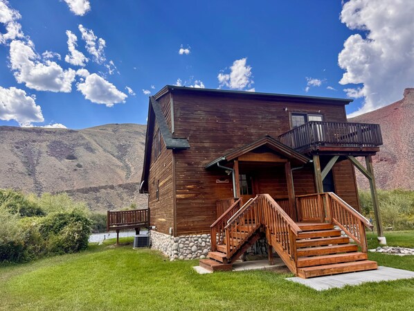 A wooden cabin with a stone foundation, a wooden staircase, and a deck.