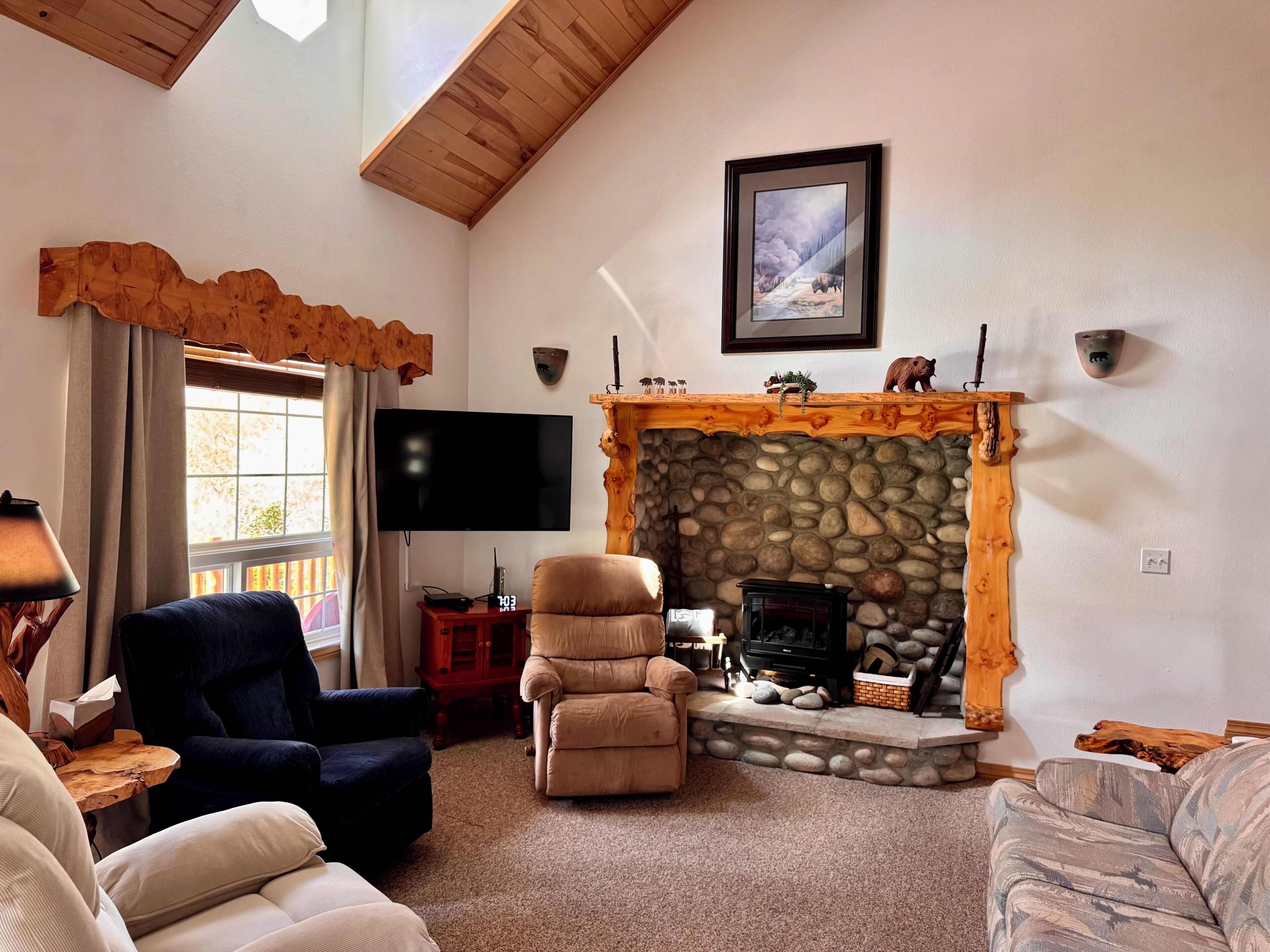 A living room with a stone fireplace, a flat-screen TV, and two sofas.