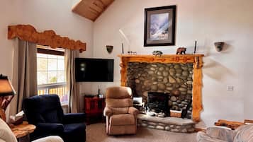 A living room with a stone fireplace, a flat-screen TV, and two sofas.