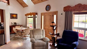 A living room with a dining area, a wooden ceiling, a clock, and a window with curtains.