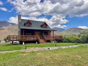 A wooden cabin with a stone chimney, a porch, and a view of mountains.
