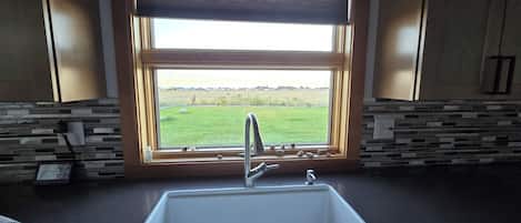 A kitchen with a window, a sink, and a view of a green field.