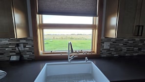 A kitchen with a window, a sink, and a view of a green field.