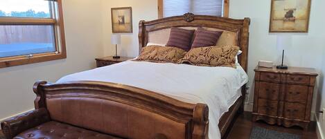 A bedroom with a large bed, a ceiling fan, a nightstand, a dresser, and a window with blinds.