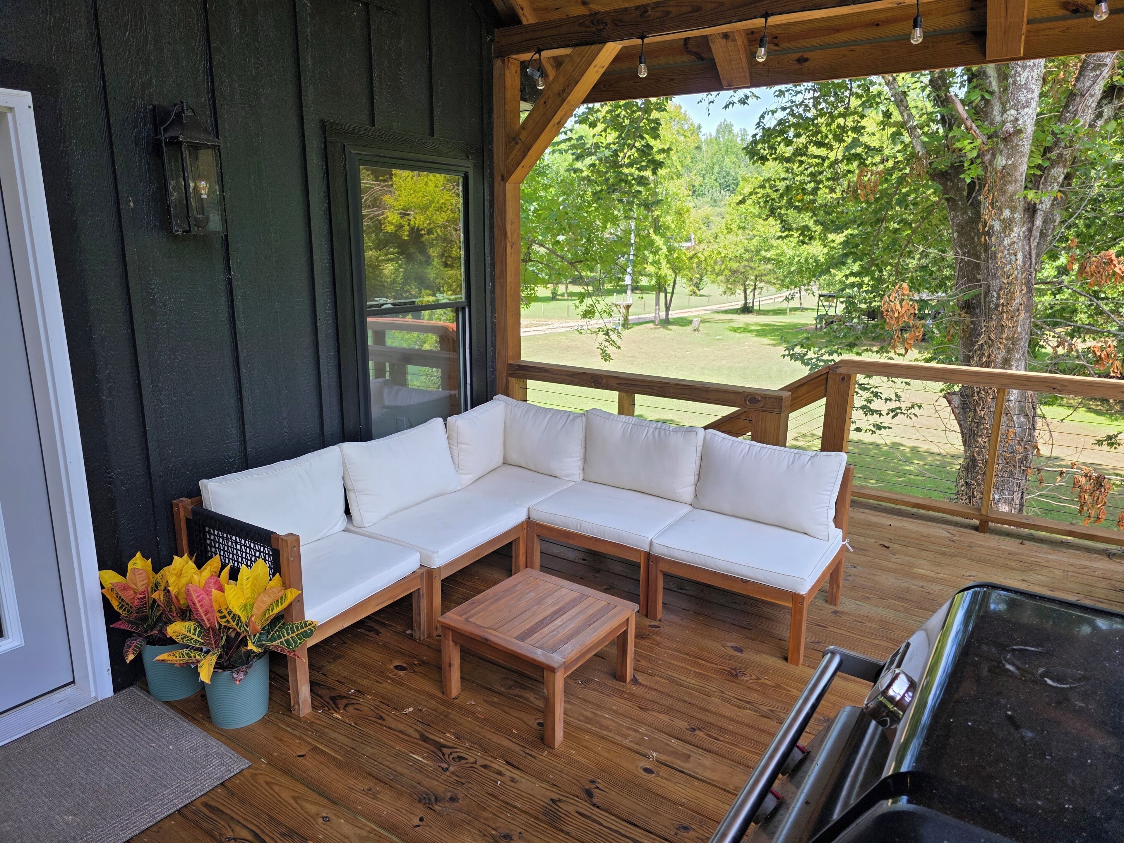 Un espace extérieur abrité, aménagé avec un banc en bois, un canapé blanc et des plantes en pot.