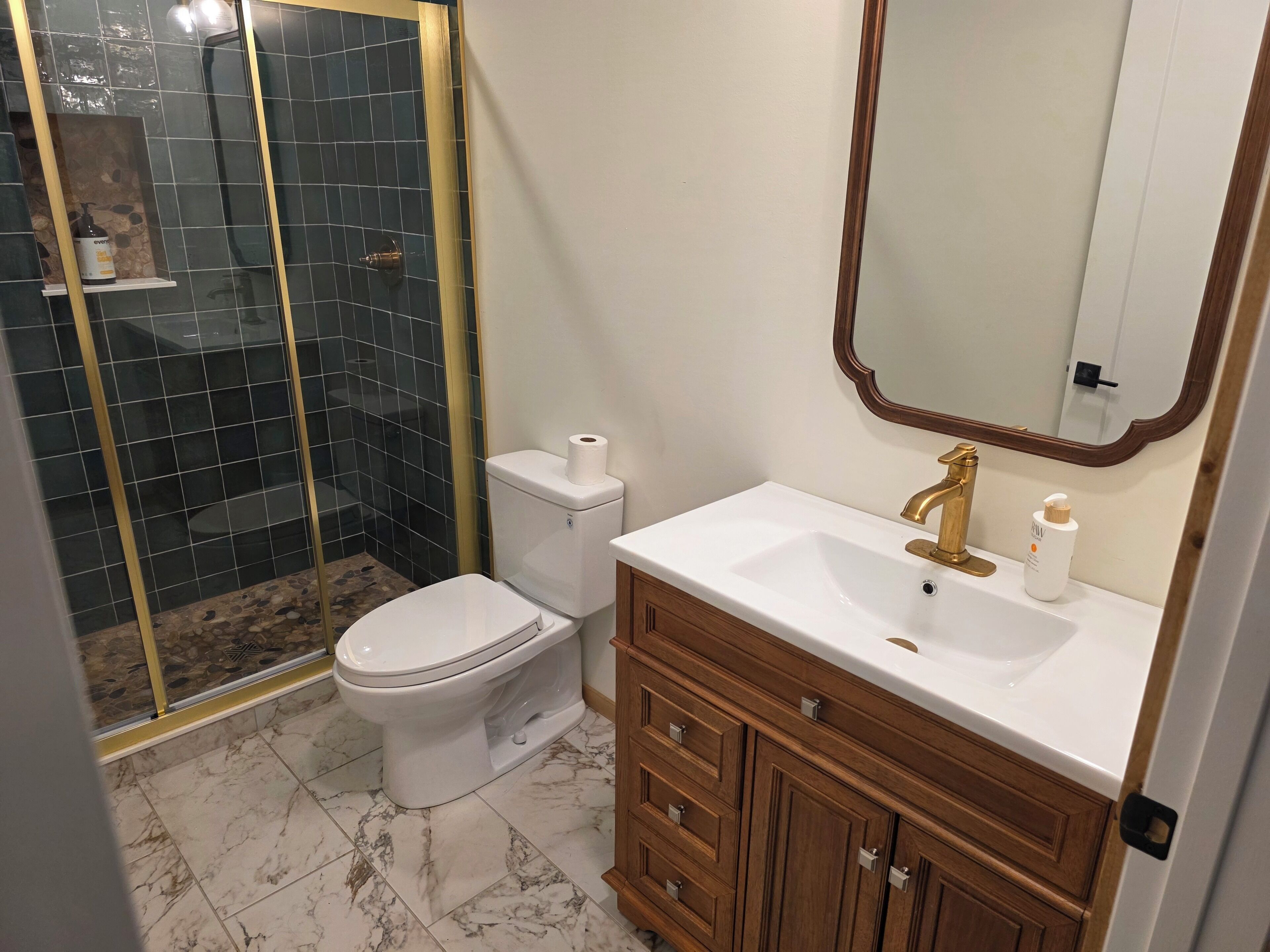 A bathroom with a toilet, a sink, a mirror, and a shower enclosure.