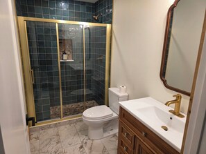 A bathroom with a glass-enclosed shower, a toilet, a sink with a gold faucet, and a mirror. - Charming 2-bedroom cabin on the water with AC in Linden (Linden)