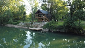 A cabin with a deck extending over a body of water, surrounded by trees.