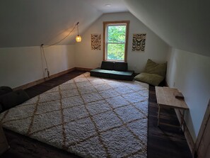 A small attic room with a sloped ceiling, a large rug, a bench, a small table, and two butterfly wall art pieces.