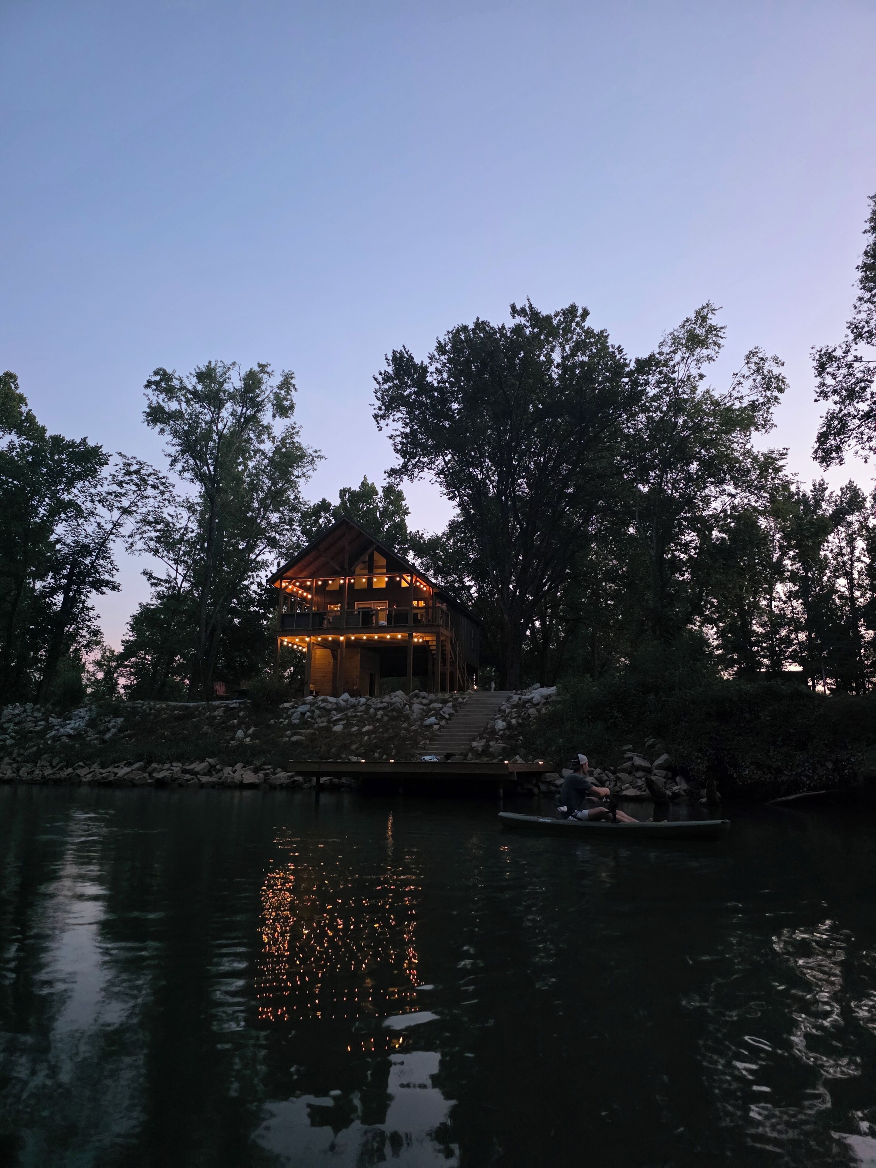 A lakeside cabin with a wooden deck and a small boat docked nearby.