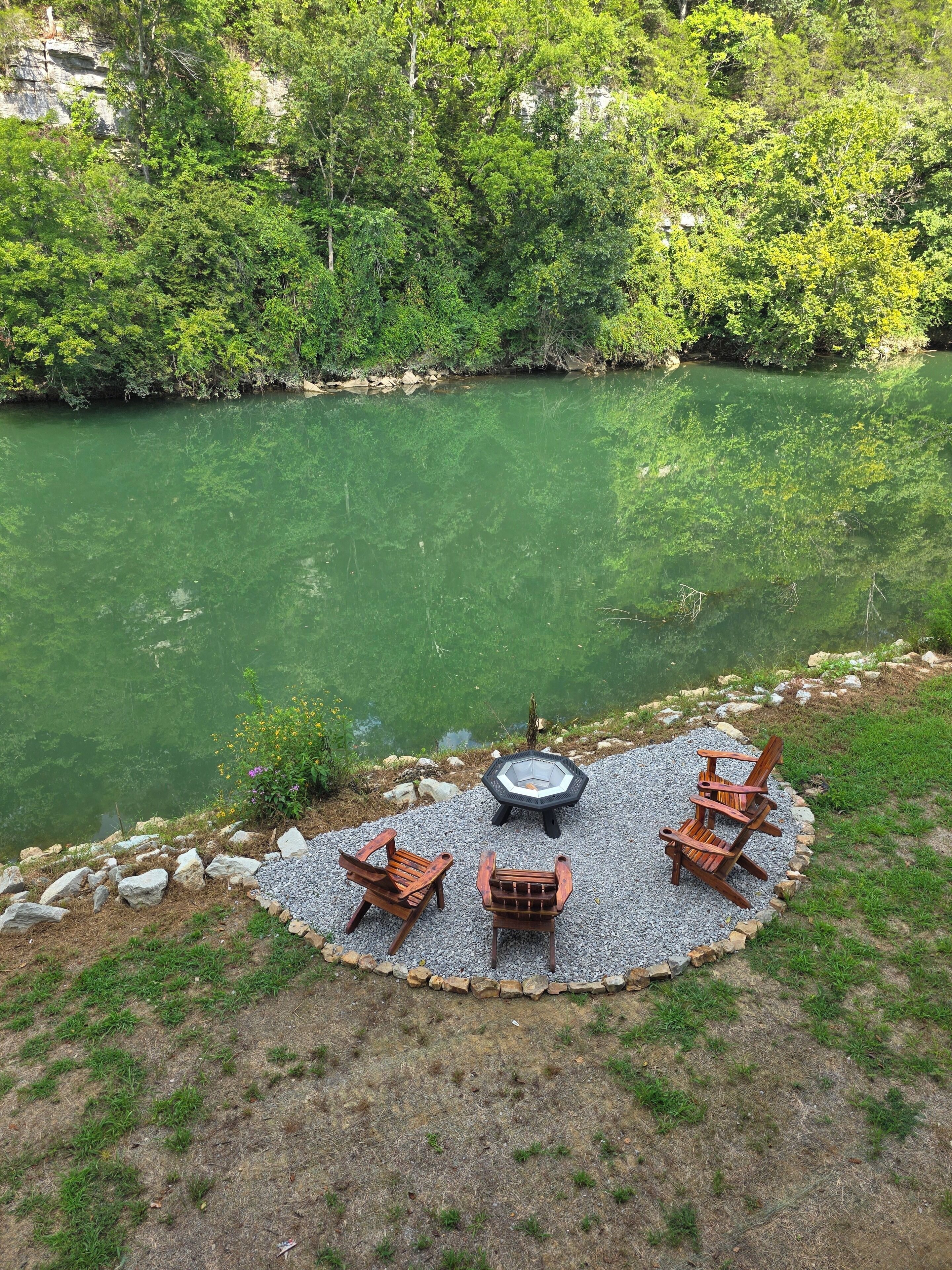 A circular outdoor seating area with a fire pit, surrounded by a gravel border, overlooking a river.