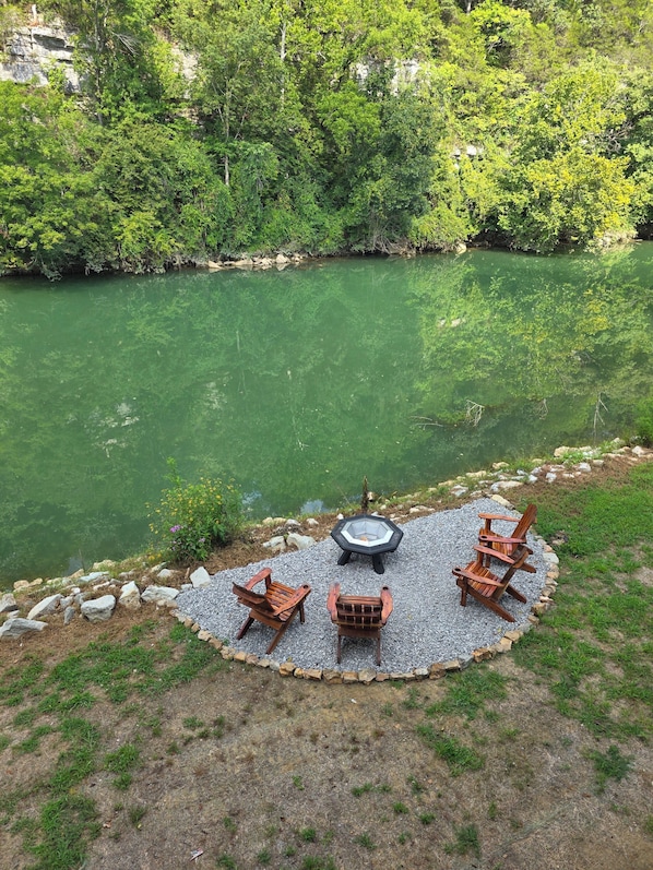 A circular outdoor seating area with a fire pit, surrounded by a gravel border, overlooking a river.