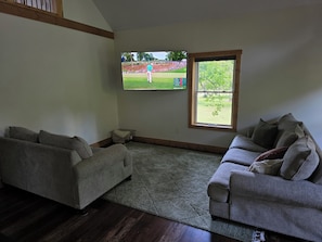 A living room with two grey sofas, a patterned rug, a wooden floor, and a TV displaying a golf course.